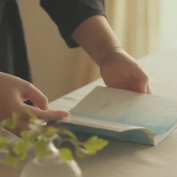 一雙手翻開桌上的書，旁邊是一盆綠色植物